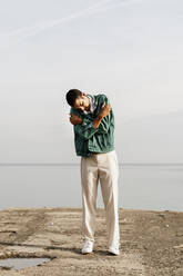 Young man self hugging against sky and sea - AFVF07850