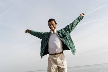 Smiling man with arms outstretched against sea - AFVF07856