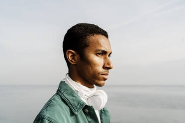 Junger Mann mit Kopfhörern blickt über Meer und Himmel hinweg - AFVF07861
