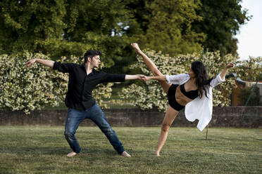 Tänzerpaar hält sich an der Hand und tanzt über Gras im Hinterhof - MAUF03665