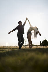 Female dancer dancing on tiptoe while holding hand of male dancer in field - MAUF03673