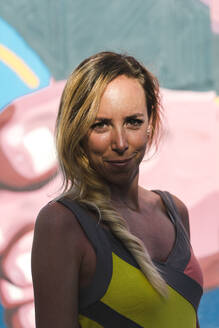 Mid erwachsene Frau mit blondem Haar gegen grafittin Wand auf sonnigen Tag - JMPF00728