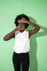 Frau, die ihr Gesicht mit den Händen bedeckt, während sie vor einem grünen Hintergrund steht - GIOF09946