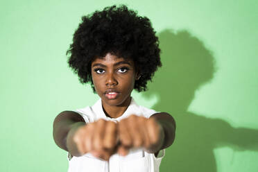 Young woman showing fist while standing against green background - GIOF09956