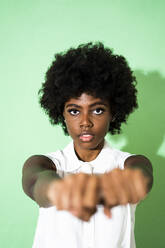 Woman showing fist while standing against green background - GIOF09957