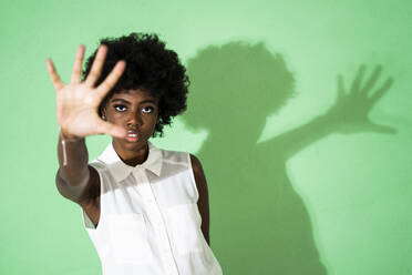 Curly hair woman showing stop gesture while standing against green background - GIOF09958