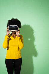 Junge Frau benutzt ein Virtual-Reality-Headset, während sie vor einem grünen Hintergrund steht - GIOF09960