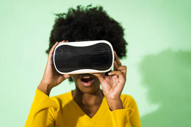 Frau mit offenem Mund, die ein Virtual-Reality-Headset benutzt, während sie vor einem grünen Hintergrund steht - GIOF09961