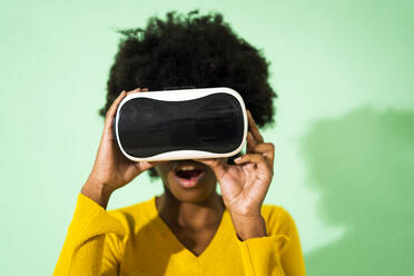 Woman with mouth open using virtual reality headset while standing against green background - GIOF09961