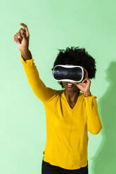 Junge Frau, die einen Virtual-Reality-Simulator benutzt, steht mit erhobener Hand vor grünem Hintergrund - GIOF09962