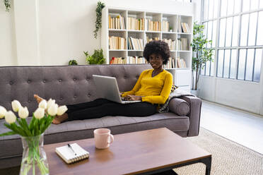 Young woman using laptop while sitting on sofa at home - GIOF09973