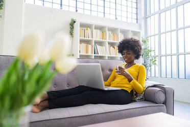 Woman drinking coffee while working on laptop at home - GIOF09974