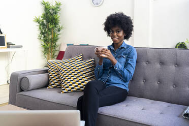 Lächelnde Frau trinkt Kaffee, während sie zu Hause sitzt - GIOF09982
