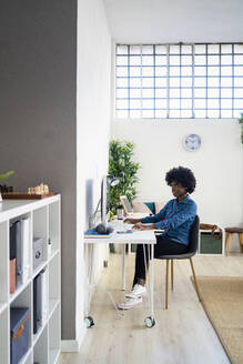 Frau arbeitet am Computer, während sie zu Hause im Büro sitzt - GIOF09993