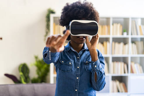 Frau mit Virtual-Reality-Headset, die ihre Hand ausstreckt, während sie zu Hause steht - GIOF10001