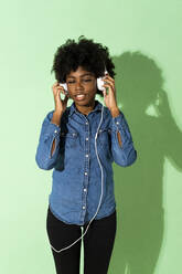 Woman wearing headphones listening music while standing against green background - GIOF10016