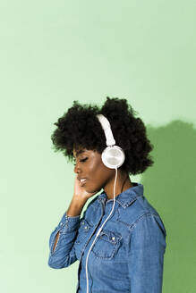 Young woman wearing headphones standing against green background - GIOF10017