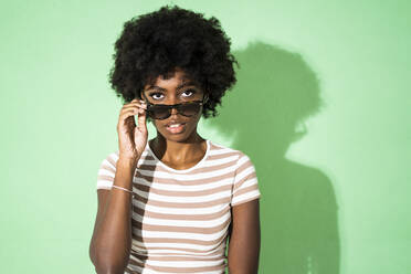 Woman with sunglasses staring while standing against green background - GIOF10034