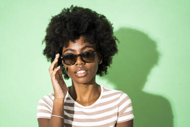 Woman adjusting sunglasses while standing against green background - GIOF10038