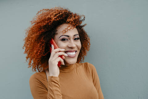 Glückliche Frau, die mit ihrem Handy telefoniert, während sie an einer grauen Wand steht, lizenzfreies Stockfoto