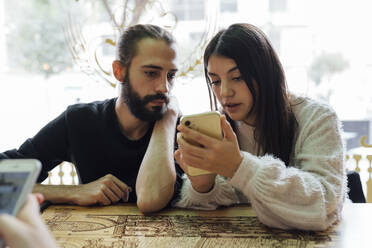 Junge Freunde benutzen ihr Smartphone, während sie im Restaurant sitzen - EGAF01274