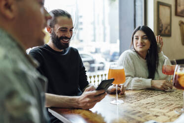 Male and female friends with drinks at table in bar - EGAF01279