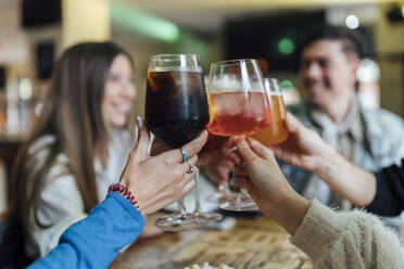 Freunde stoßen mit einem Getränk über dem Tisch in einer Bar an - EGAF01282