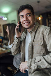 Lächelnder Mann, der in einer Bar mit dem Handy telefoniert und dabei wegschaut - EGAF01293