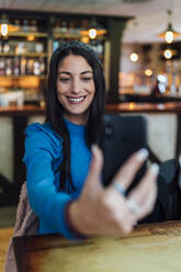 Attractive woman taking selfie on smart phone in bar - EGAF01294