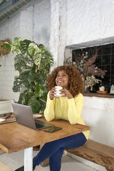 Smiling businesswoman day dreaming while holding coffee cup in cafe - VEGF03320