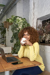 Happy female entrepreneur having coffee while looking away in coffee shop - VEGF03321