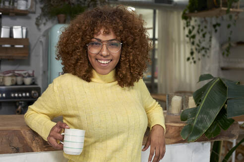 Lächelnde Frau mit Kaffeetasse an der Theke eines Cafés lehnend - VEGF03325