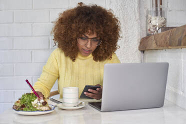 Freiberufliche Mitarbeiterin schreibt auf einem Notizblock, während sie in einem Café telefoniert - VEGF03331