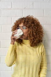 Woman drinking coffee while looking away against brick wall - VEGF03332