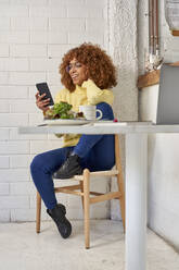 Happy businesswoman using smart phone while sitting on chair in cafe - VEGF03337