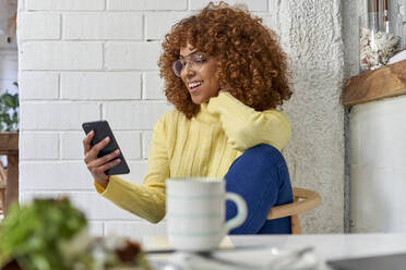 Happy female entrepreneur with coffee cup checking mobile phone in cafe - VEGF03338