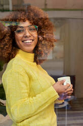 Lächelnde Frau mit Kaffeetasse träumt hinter Glas in einem Cafe - VEGF03340