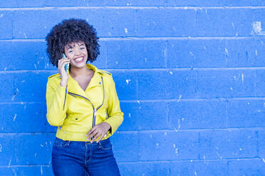 Smiling fashionable woman on phone call against blue wall - GGGF00490