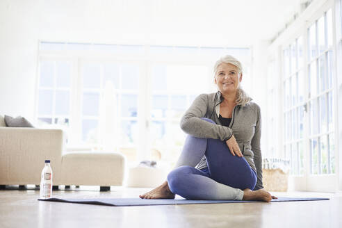 Smiling senior woman doing exercise on mat in living room - JAHF00001