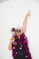 Cheerful senior woman with hands raised enjoying drink against white background - JAHF00025