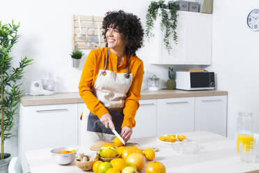 Happy woman looking away while cutting fruit standing in kitchen at home - GIOF10044