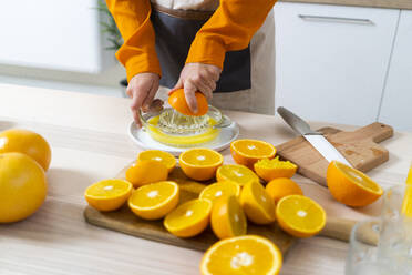 Frau, die eine Orange in der Saftpresse auspresst, während sie in der Küche zu Hause Saft zubereitet - GIOF10049