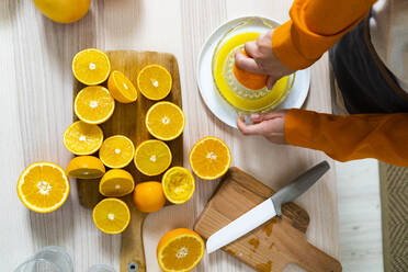 Frau bereitet Orangensaft in einer Saftpresse zu, während sie zu Hause am Tisch steht - GIOF10050