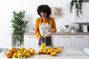 Frau gießt Orangensaft in eine Flasche, während sie in der Küche steht - GIOF10051