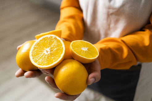 Frau hält Orange und Orangenscheibe in der Hand, während sie zu Hause steht - GIOF10073