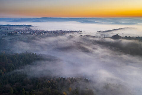 Deutschland, Baden-Württemberg, Berglen, Drohnenansicht eines in dichten Nebel gehüllten Dorfes in der Morgendämmerung, lizenzfreies Stockfoto