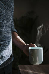 Man holding hot cup of coffee while standing at home - EBBF01790