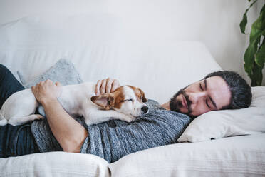 Mann schläft mit Hund auf dem Sofa zu Hause - EBBF01797