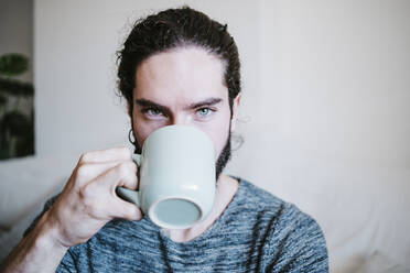 Man with blue eyes staring while drinking coffee sitting at home - EBBF01810