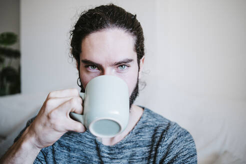 Mann mit blauen Augen starrt beim Kaffeetrinken zu Hause sitzend - EBBF01810